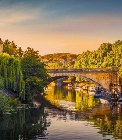 Beautiful view of the River Avon in Bath with a stone bridge and boats along the riverside at golden hour, Near Brokerswood Holiday Park.