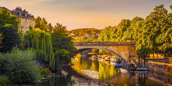 Beautiful view of the River Avon in Bath with a stone bridge and boats along the riverside at golden hour, Near Brokerswood Holiday Park.
