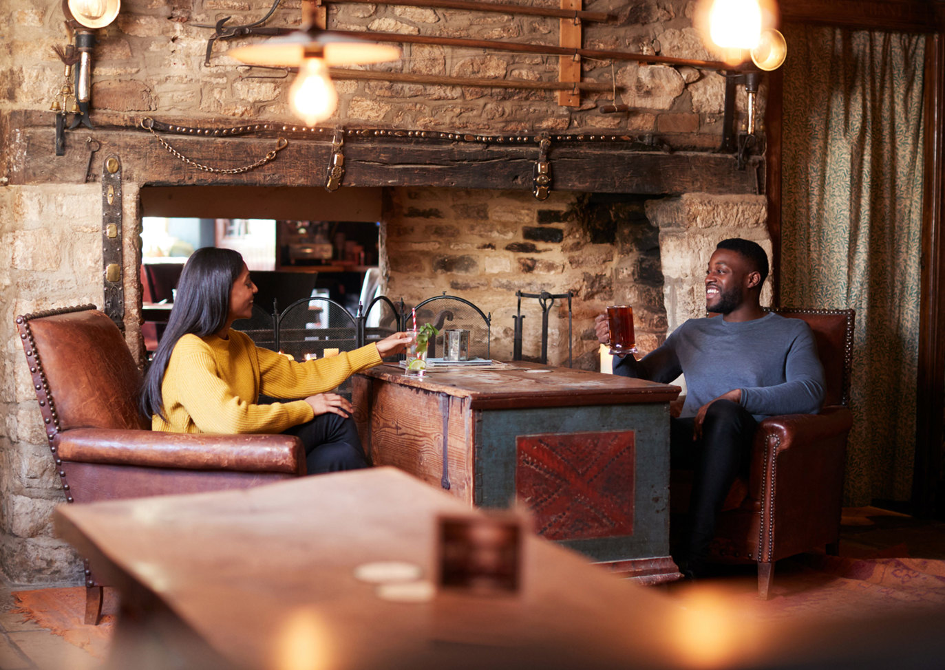 Couple relaxing with drinks inside a cosy traditional English pub with rustic stone walls, Near Brokerswood Holiday Park.