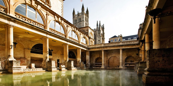 The ancient Roman Baths in Bath, with steaming waters surrounded by classical stone columns, Near Brokerswood Holiday Park.