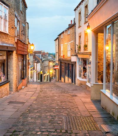 Historic cobbled street in Frome, Somerset, lined with quaint shops and evening lights, Near Brokerswood Holiday Park.