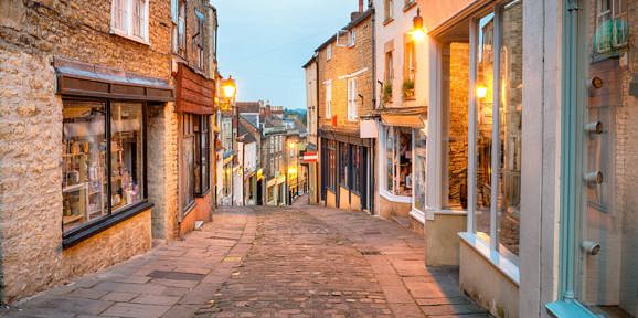 Historic cobbled street in Frome, Somerset, lined with quaint shops and evening lights, Near Brokerswood Holiday Park.