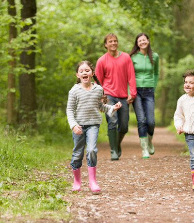 Happy family enjoying a woodland walk with children running ahead on a forest trail, Near Brokerswood Holiday Park.