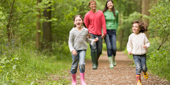 Happy family enjoying a woodland walk with children running ahead on a forest trail, Near Brokerswood Holiday Park.