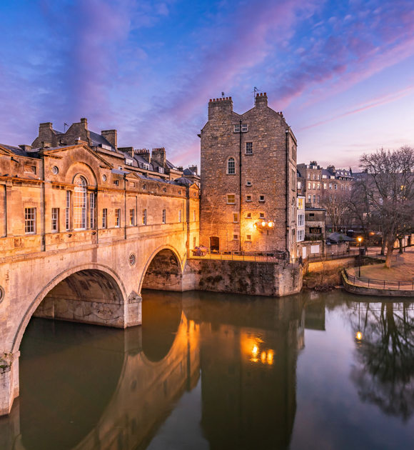 Scenic evening view of Bath with Pulteney Bridge and riverside buildings glowing in warm light, Near Brokerswood Holiday Park.