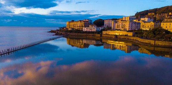 Coastal view of Weston-super-Mare at sunset golden hour, buildings reflecting on the calm water, Near Brokerswood Holiday Park.
