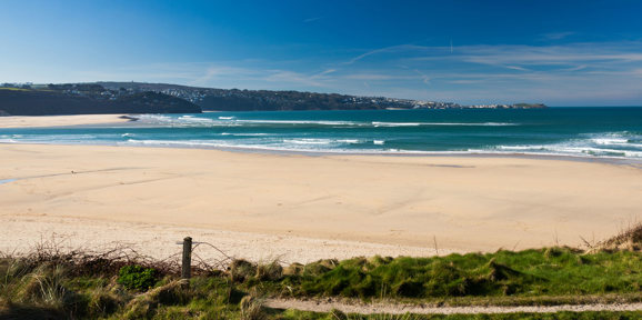 Wide sandy expanse of Hayle Towans Beach with waves and blue skies, near Praa Sands Holiday Park.