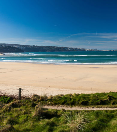 Wide sandy expanse of Hayle Towans Beach with waves and blue skies, near Praa Sands Holiday Park.