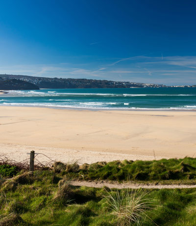 Wide sandy expanse of Hayle Towans Beach with waves and blue skies, near Praa Sands Holiday Park.