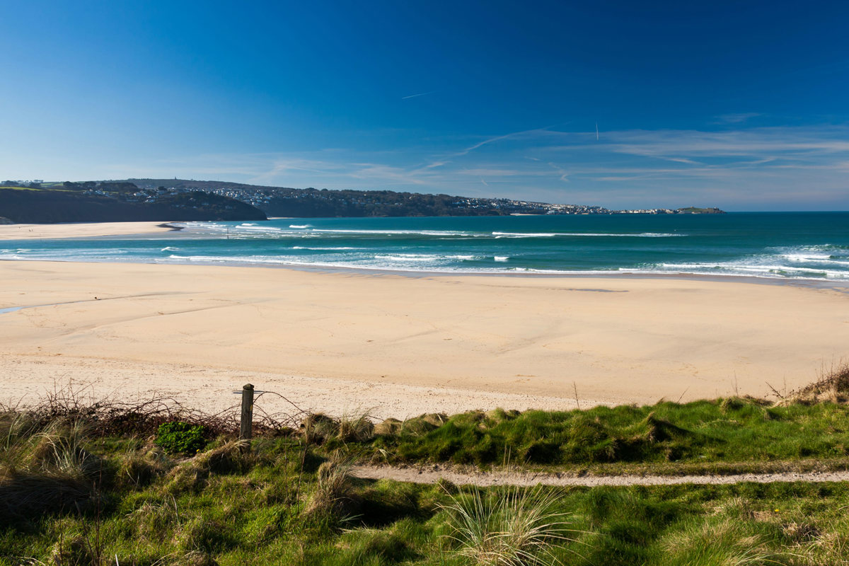 Wide sandy expanse of Hayle Towans Beach with waves and blue skies, near Praa Sands Holiday Park.