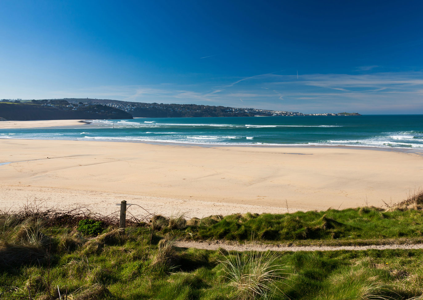 Wide sandy expanse of Hayle Towans Beach with waves and blue skies, near Praa Sands Holiday Park.