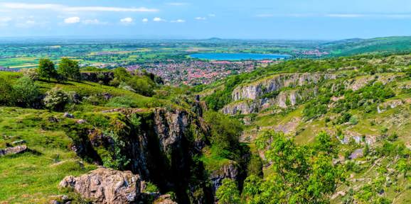 Panoramic daytime view of Cheddar Gorge with rocky cliffs and green countryside stretching into the distance, Near Brokerswood Holiday Park.