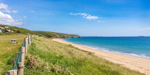 Scenic view of Praa Sands beach with golden sand, grassy dunes, and turquoise sea near Praa Sand Holiday Park.