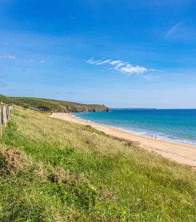 Scenic view of Praa Sands beach with golden sand, grassy dunes, and turquoise sea near Praa Sand Holiday Park.