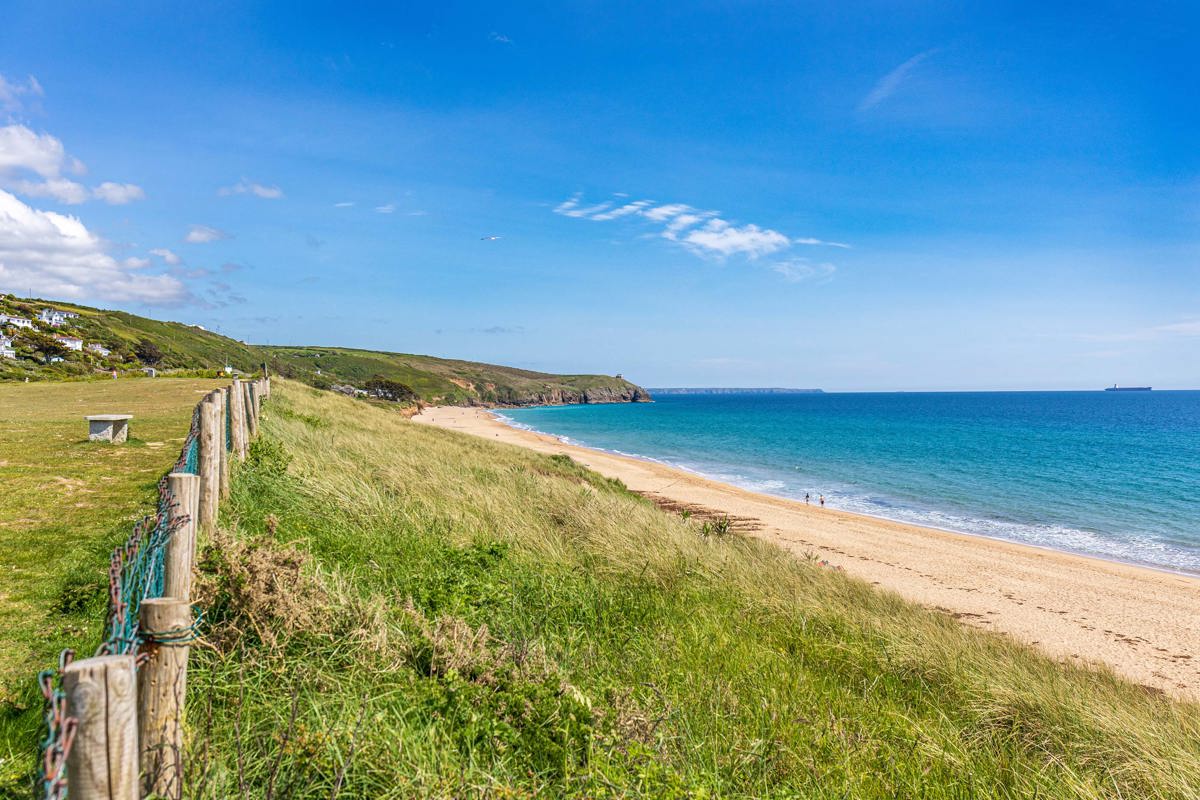 Scenic view of Praa Sands beach with golden sand, grassy dunes, and turquoise sea near Praa Sand Holiday Park.