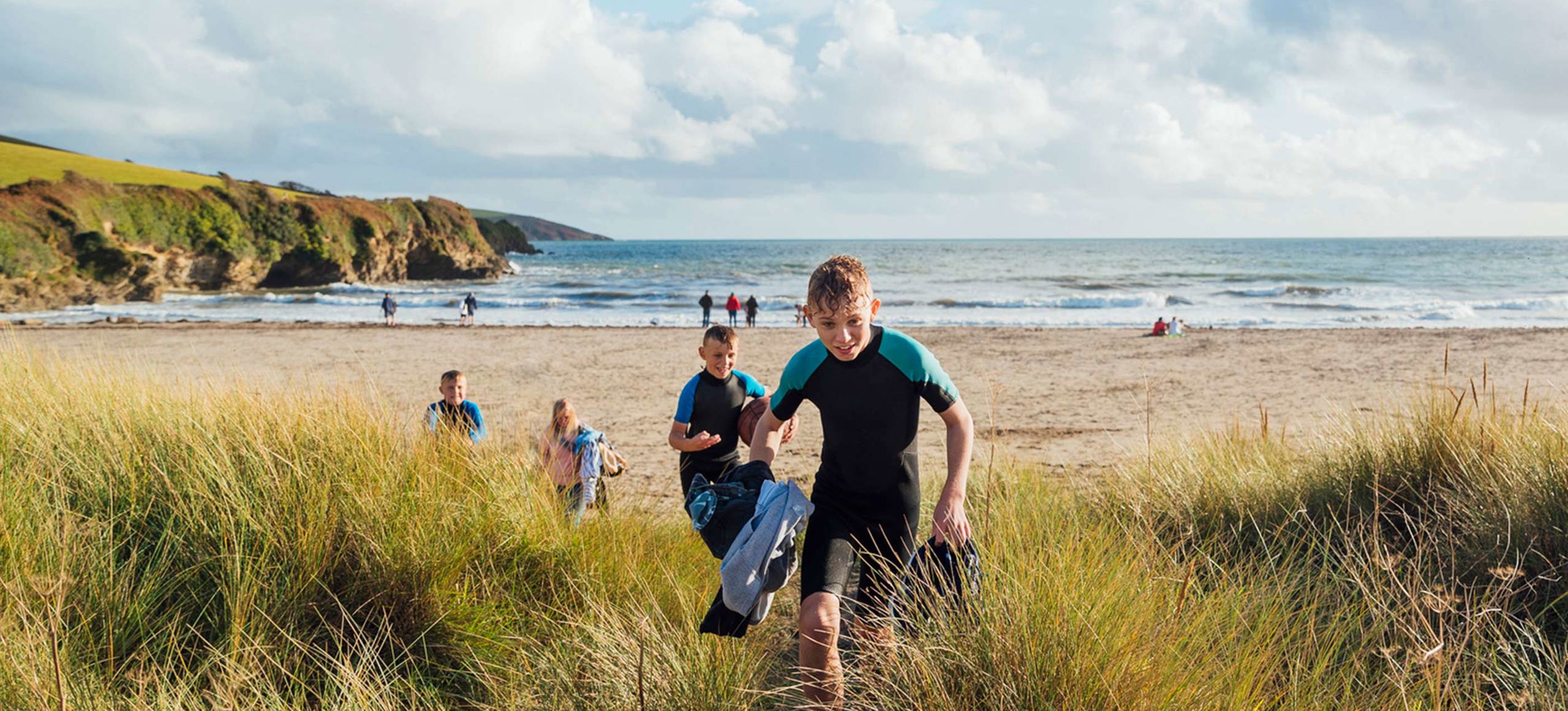 Children in wetsuits walking through sand dunes towards the beach near Praasand Holiday Park.