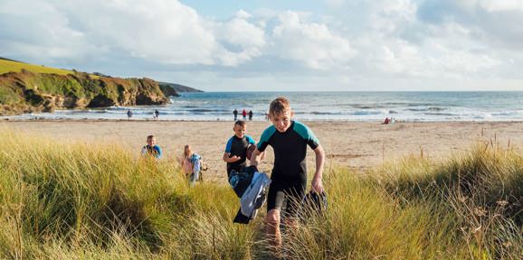 Children in wetsuits walking through sand dunes towards the beach near Praasand Holiday Park.
