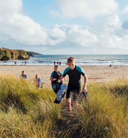 Children in wetsuits walking through sand dunes towards the beach near Praasand Holiday Park.