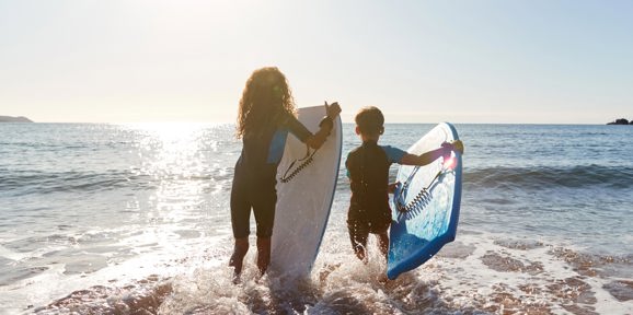 ids carrying surfboards into the sea on a sunny day near Praa Sand Holiday Park.