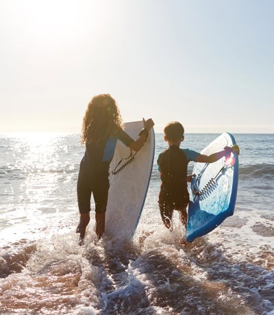 ids carrying surfboards into the sea on a sunny day near Praa Sand Holiday Park.