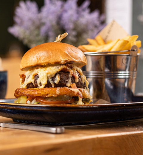 Gourmet cheeseburger served with fries on a rustic table in Boathouse restaurant at Praa Sands Holiday Park.
