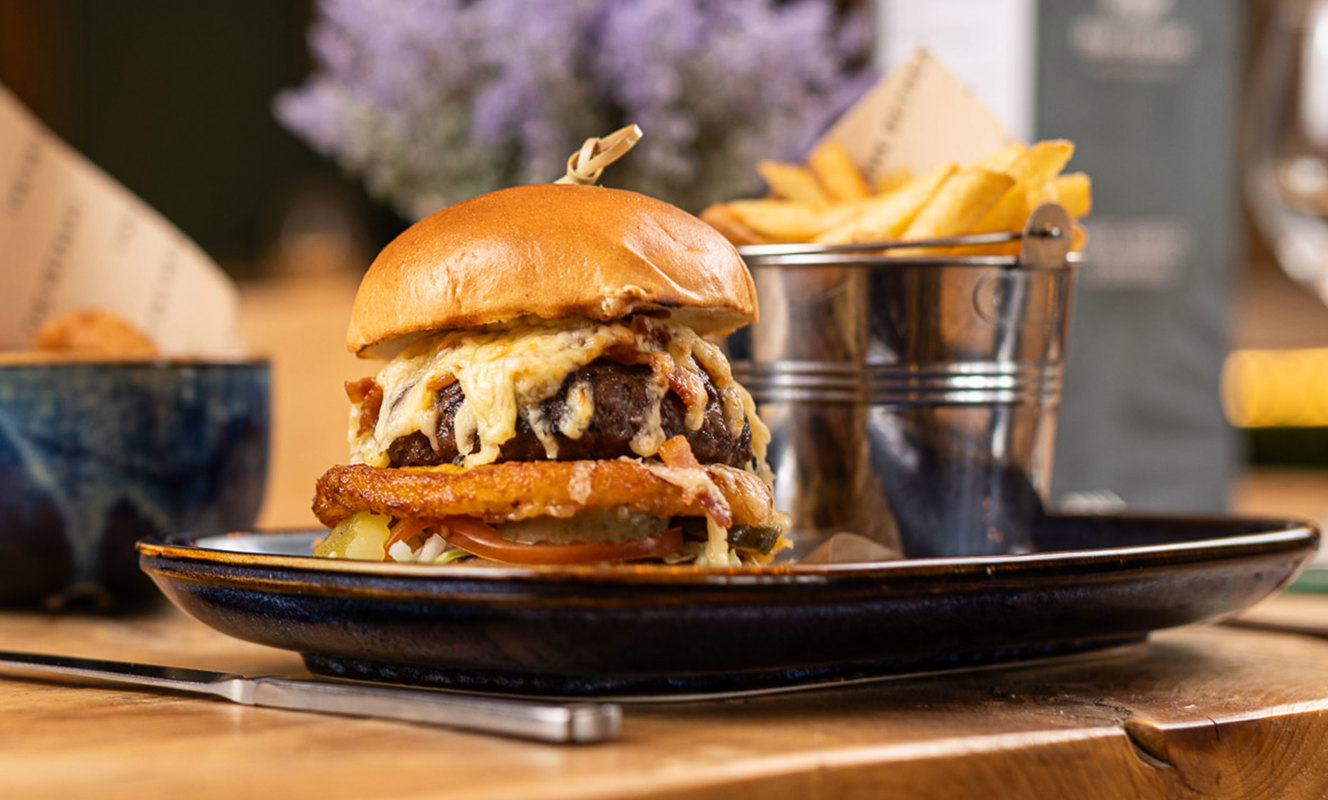 Gourmet cheeseburger served with fries on a rustic table in Boathouse restaurant at Praa Sands Holiday Park.