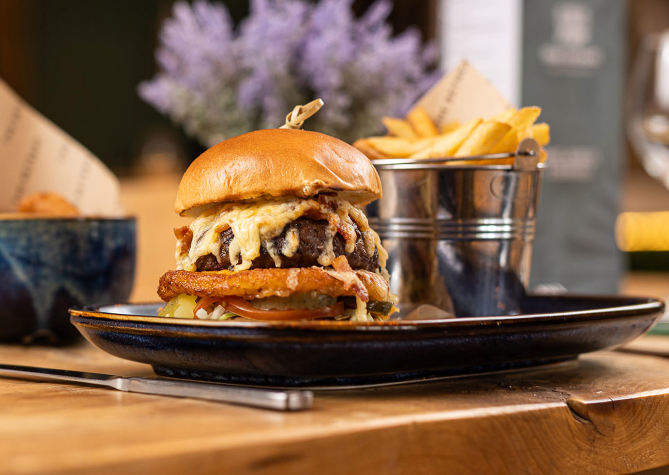 Gourmet cheeseburger served with fries on a rustic table in Boathouse restaurant at Praa Sands Holiday Park.